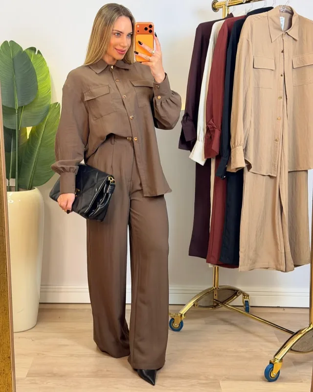 Modelo usando conjunto de camisa e calça pantalona marrom, com outras cores na arara